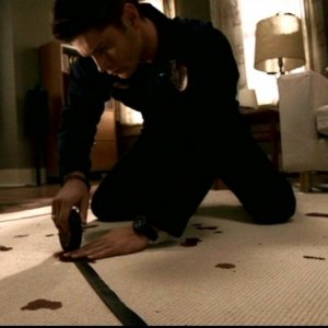 Jensen Ackles nel ruolo di Dean, ricostruisce un simbolo con del nastro adesivo, nell'appartamento dell'ultima vittima nell'episodio 'Ombre' di Supernatural