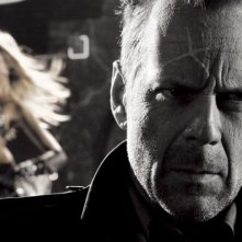 Un primo piano di Bruce Willis con alle spalle Jessica Alba in una scena di Sin City