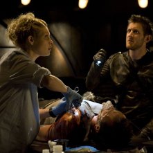 Koz (Primo Allon) fa luce a TJ (Alaina Kalanj) mentre opera Varro (Mike Dopud) nell'episodio Incursion: Part 2 di Stargate Universe