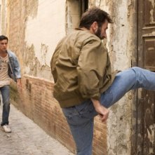 Antonio De La Torre sfonda una porta a calci in Grupo 7. Dietro di lui, Mario Casas