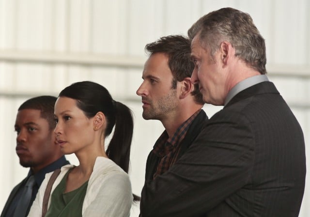 Jonny Lee Miller insieme a Jon Michael Hill, Aidan Quinn e Lucy Liu in una scena dell'episodio Flight Risk della prima stagione di Elementary