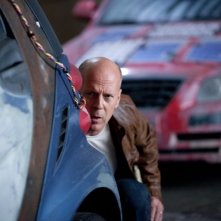 Bruce Willis appostato dietro un'auto in una scena di Looper