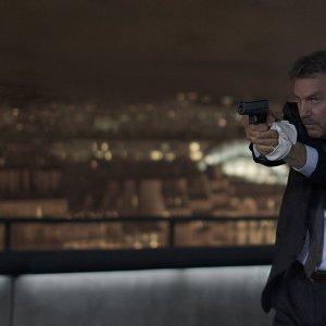 3 Days to Kill: Kevin Costner in una scena d'azione del film punta la sua pistola
