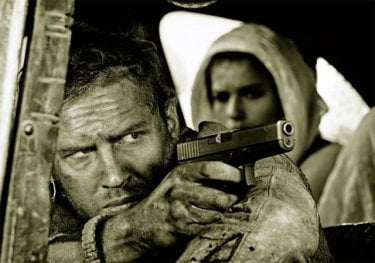 Mad Max: Fury Road - Un primo piano di Tom Hardy menytre impugna la pistola