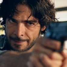 L'esigenza di unirmi ogni volta con te: un primo piano di Marco Bocci con una pistola in mano